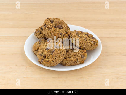 Several oatmeal chocolate chip cookies on a white plate atop a wood table. Stock Photo