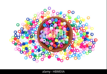 A small clay bowl filled with colorful pony beads plus scattered beads surrounding the dish isolated on a white background. Stock Photo