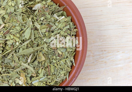 Top close view of a small bowl filled with cut and sifted dried senna leaf atop a wood table. Stock Photo