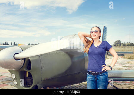 Young happy woman standing near sport plane on airfield delighted before flight. Stock Photo