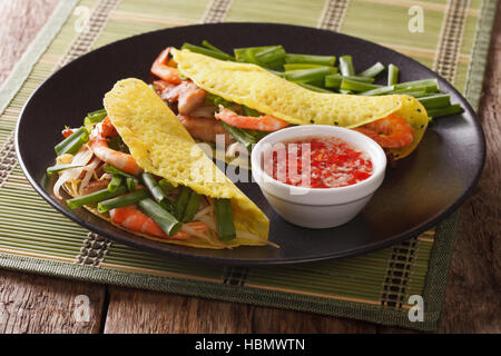 Banh Xeo rice crepes with pork, shrimp, onions and bean sprouts and a Nuoc Cham spicy sauce closeup on a plate on the table. horizontal Stock Photo