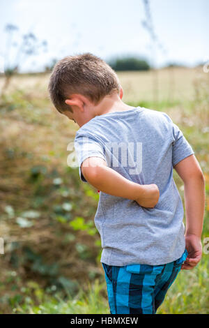 child scratching his back on a country road Stock Photo