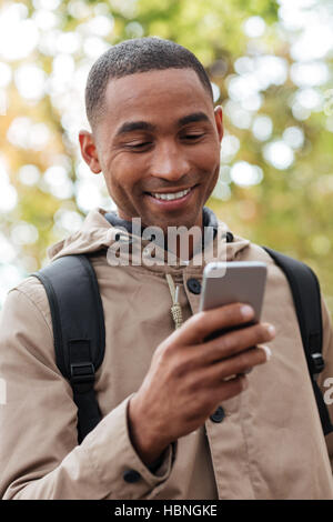 Image of cheerful young african man holding his cellphone in hands and chatting Stock Photo