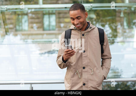 Picture of happy young african man holding his cellphone in hands and chatting Stock Photo