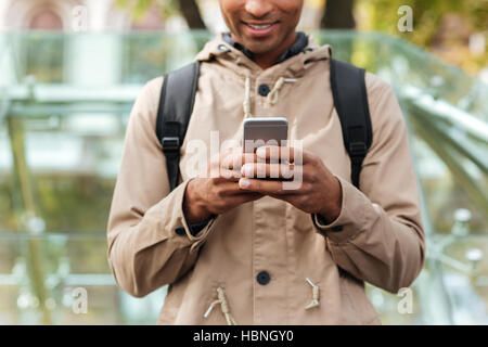 Cropped image of young dark skinned man with backpack using his cellphone on the street. Stock Photo