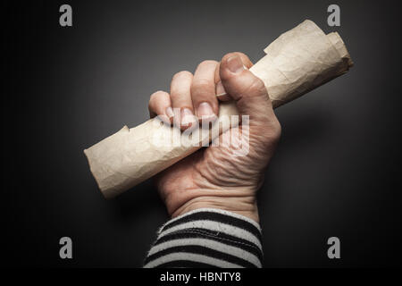 Strong sailor hand holds rolled old crumpled paper sheet over black background, pirate map  concept Stock Photo