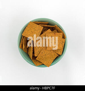 Top view of gourmet teff whole grain snack crackers in a green bowl on a white tablecloth. Stock Photo