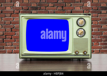 Grungy green vintage television set with brick wall and chroma key blue screen. Stock Photo