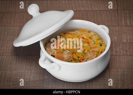 Portion of braised cabbage and homemade sausage in ceramic pot on wooden table Stock Photo