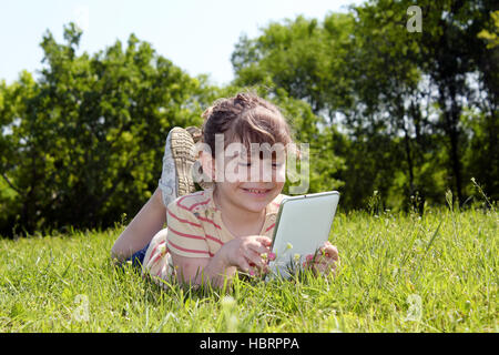 little girl lying on grass and play with tablet pc Stock Photo