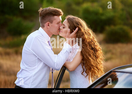 bride and groom kissing near car on wedding walk Stock Photo