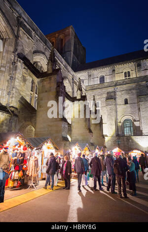 People shopping at Winchester Christmas market, by Winchester Cathedral at dusk; Winchester, Hampshire UK Stock Photo