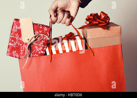 closeup of the hand of a young caucasian woman with her fingernails painted red holding a red shopping bag full of gifts wrapped in different papers Stock Photo