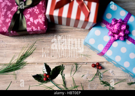 the text frohe weihnachten, merry christmas in german and some gifts wrapped in different papers and tied with ribbons of different colors, and some n Stock Photo