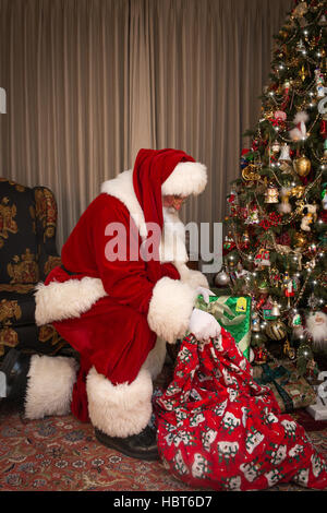 Santa Claus in living room placing gifts under Christmas tree Stock Photo