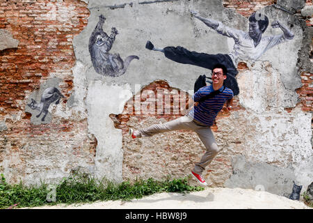 Tourist jumping in front of the wall mural titled “The Real Bruce Lee Would Never Do This”. Stock Photo