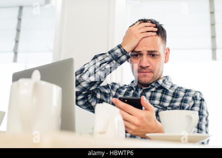 Tired handsome young freelancer is using a mobile phone while working at the coffee shop Stock Photo