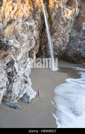 View from above of a woman walking alone on the beach towards McWay Falls on Julia Pfeiffer Burns State Park, California, USA. Stock Photo