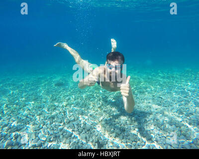 Young beard man with glasses diving in a blue clean water with thumb up Stock Photo