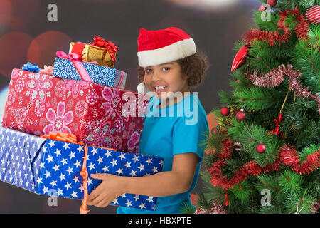 Cute little boy in santa hat holding gift near Christmas tree. Stock Photo
