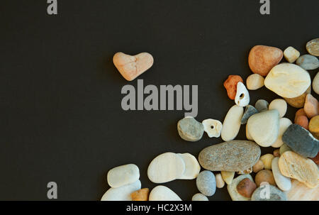 Pink stone like heart shape and a lot of different pebble on the black background Stock Photo