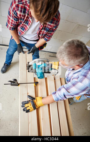 Older carpenter cutting wooden planks using jigsaw Stock Photo