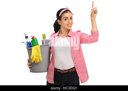 Young woman holding a bucket filled with cleaning products and pointing up isolated on white background Stock Photo