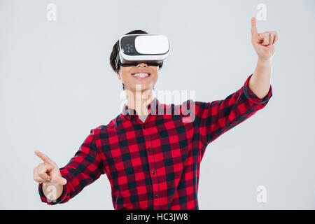 Image of asian man dressed in casual shirt in a cage and wearing virtual reality device and pointing. Isolated over white background. Stock Photo