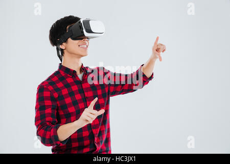 Asian man dressed in casual shirt in a cage and wearing virtual reality device and pointing. Isolated over white background. Stock Photo