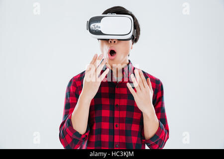 Photo of surprised asian man dressed in casual shirt in a cage and wearing virtual reality device. Isolated over white background. Stock Photo