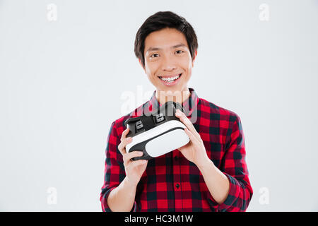 Photo of young man dressed in casual shirt in a cage and holding virtual reality device. Isolated over white background. Stock Photo