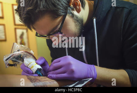 Tattoo artist in the process of tattooing. Soft focus. Focus on the hands of the artist. Stock Photo