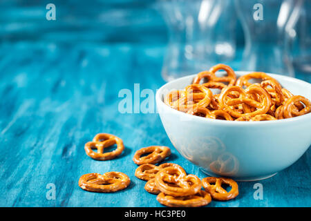 Salty snacks mini pretzels in bowl on blue wooden table Stock Photo