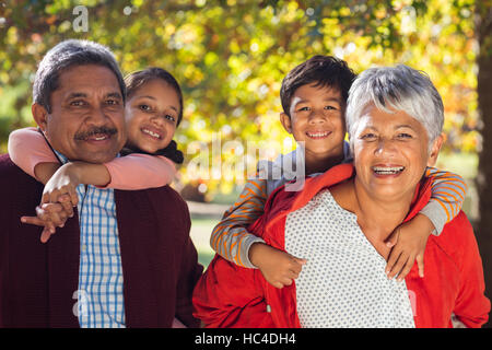 Happy grandparents piggybacking grandchildren at park Stock Photo