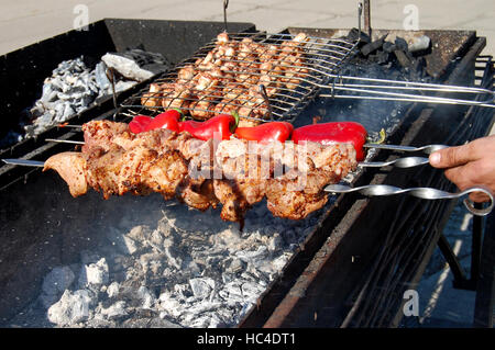 Preparation of barbecue meat shish kebab on skewers grill food. Man grilling traditional summer picnic marinated pork on coal ember brazier. Concept o Stock Photo