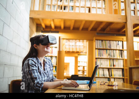 Female student using laptop and virtual reality headset in library Stock Photo