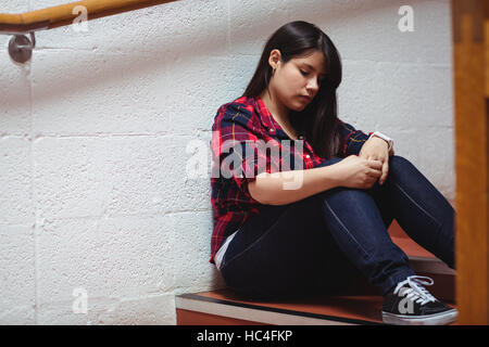 Upset female student sitting on staircase Stock Photo