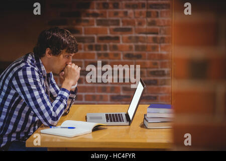 Thoughtful student using laptop in library Stock Photo
