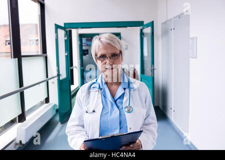 Confident female doctor with clipboard standing in hospital corridor Stock Photo