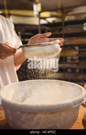Mid-section of female baker sifting flour through a sieve Stock Photo