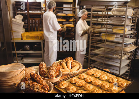 Michetta and sweet food on a table while male and female baker working in background Stock Photo