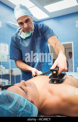 Male surgeon resuscitating an unconscious patient with a defibrillator Stock Photo