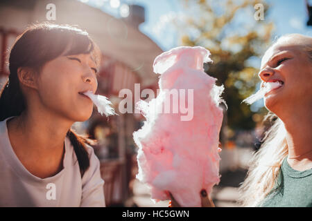 Two young women sharing cotton candyfloss at amusement park. Best friends eating cotton candy together outdoors.