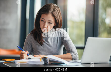 Shot of young woman taking down notes in diary. Female university student preparing note for the exam at library. Stock Photo