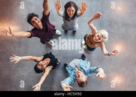 Top view of young students standing together looking up at camera with their hands raised in celebration. Stock Photo