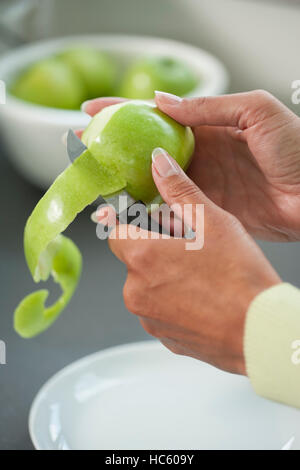 Two hands of a woman using knife to peeli an apple skin. Close up Stock Photo