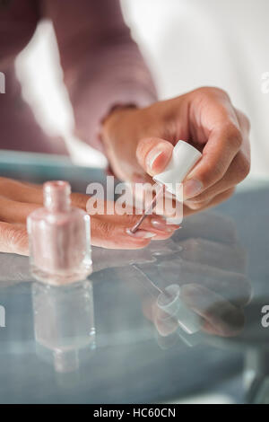 Beautiful woman at home making a pause to painting her nails on a green glass table Stock Photo