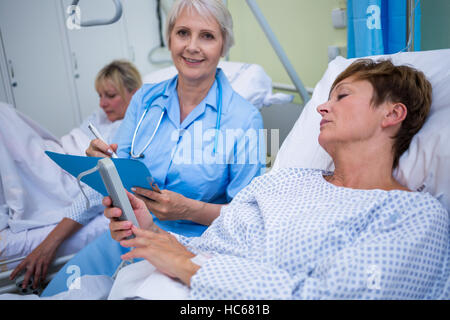 Patient using medical device and nurse sitting next to the bed Stock Photo