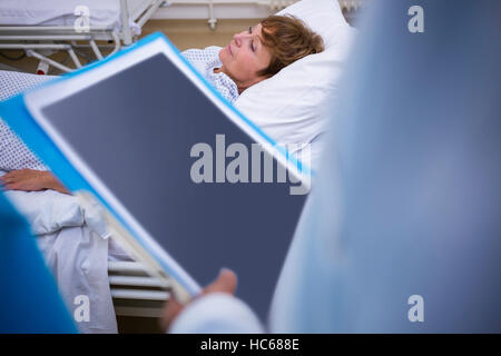 Patient lying on bed while doctor holding medical report Stock Photo