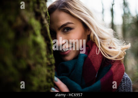 Beautiful woman hiding behind tree trunk in forest Stock Photo